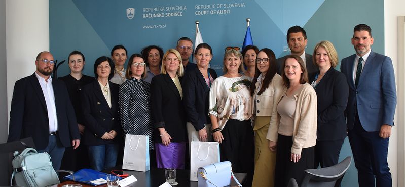 Skupinska fotografija Skupinska fotografija udeležencev študijskega obiska predstavnikov lokalnih uprav iz Bosne in Hercegovine na Računskem sodišču Republike Slovenije. Udeleženci stojijo v sejni sobi pred ozadjem z logotipom Računskega sodišča ter zastavama Slovenije in Evropske unije.