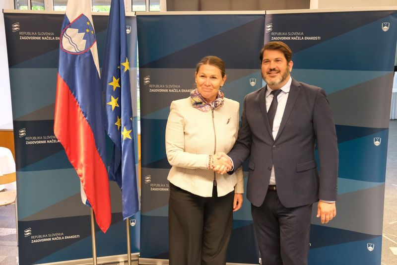 Jana Ahčin in Miha Lobnik se rokujeta ob slovenski in evropski zastavi.