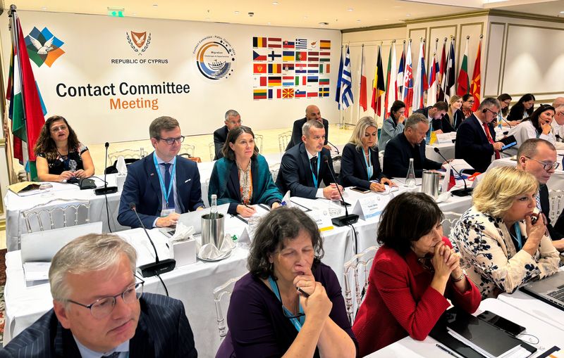 Udeleženci letnega srečanja Kontaktnega odbora sedijo v dvorani in sledijo razpravam o ključnih temah, kot so migracijska politika in neodvisnost vrhovnih revizijskih institucij. Za udeleženci so izobešene zastave držav.