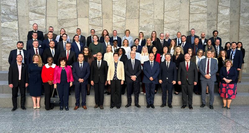 Skupinska fotografija udeležencev Skupinska fotografija udeležencev rednega srečanja predstavnikov pristojnih nacionalnih revizijskih organov (CNAB) in članov Mednarodnega revizijskega odbora za NATO (IBAN), ki je 21. maja 2026 potekalo na sedežu zveze NATO v Bruslju. Na fotografiji je približno 60 udeležencev, žensk in moških v poslovnih oblačilih, razporejenih v več vrstah na stopnicah pred veliko kamnito steno svetlih sivih tonov. V ospredju stojijo predstavniki različnih držav in institucij, med njimi tudi pomočnik vrhovne državne revizorke Računskega sodišča Republike Slovenije Viki Twrdy. Srečanje je bilo namenjeno predstavitvi dela odbora IBAN v preteklem letu ter razpravi o revizijah na področju obrambe, zaupnosti podatkov in mednarodnem sodelovanju vrhovnih revizijskih institucij.