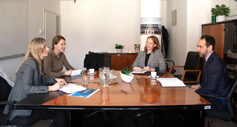 V pisarni za leseno mizo sedijo vrhovni državni revizor Luka Ramovš, njegova namestnica mag. Maša Železnik in predstavnici Urada OVSE za demokratične institucije in človekove pravice (ODIHR). Sogovorniki sedijo drug nasproti drugega ter med pogovorom pregledujejo zapiske in dokumente. Na mizi so kozarci z vodo, skodelice za kavo in pisala. V ozadju so omare z dokumenti in tabla z zapiski.