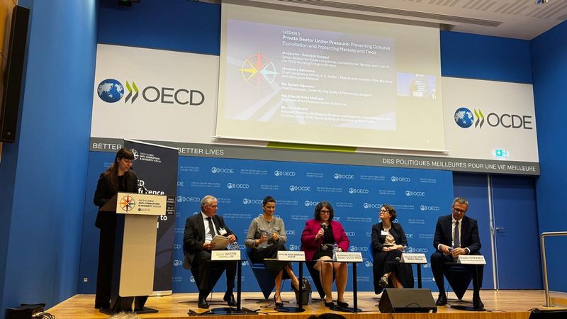 Oder z govornico in panelom več govorcev na sedežu OECD v Parizu, v ozadju projekcijsko platno z naslovom dogodka in logotipi OECD.