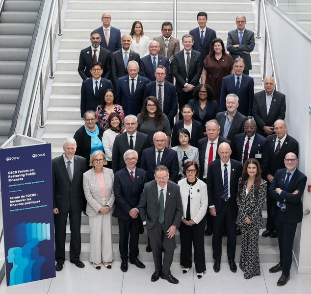 Skupinska fotografija vodij VRI držav OECD Skupinska fotografija vodij vrhovnih revizijskih institucij držav članic OECD, posneta na stopnišču v prostorih organizacije. Udeleženci, oblečeni v poslovna oblačila, so razporejeni v več vrstah in pozirajo za uradni skupinski posnetek. Ob stopnišču stoji informativni pano foruma OECD o obnovi javnih financ. Fotografija odraža mednarodno sodelovanje in izmenjavo izkušenj med najvišjimi predstavniki nacionalnih revizijskih institucij.
