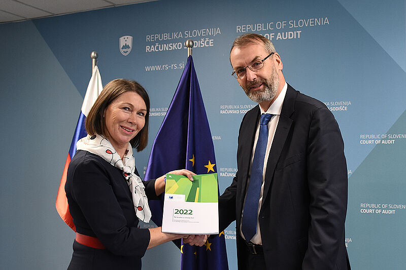 Na levi predsednica računskega sodišča, Jana Ahčin, ki sprejema letno poročilo iz rok člana evropskega računskega sodišča, magistra Jorga Kristijana Petroviča. V ozadju slovenska in evropska zastava.