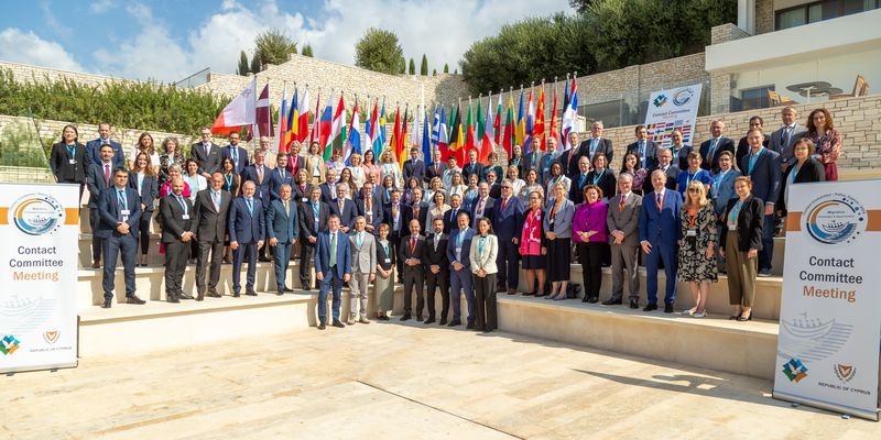 Skupinska fotografija udeležencev letnega srečanja Kontaktnega odbora na Cipru, kjer je prisotnih več kot 80 delegatov iz vrhovnih revizijskih institucij držav članic EU, Evropskega računskega sodišča in predstavnikov držav kandidatk. Udeleženci stojijo na stopnišču pred zastavami držav in oznakami dogodka.