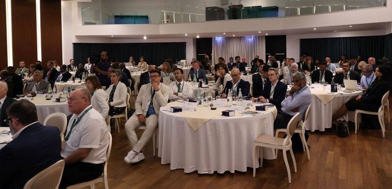Udeleženci 23. skupščine INTOSAI WGEA, sedeči za okroglimi mizami v dvorani, spremljajo plenarno zasedanje.