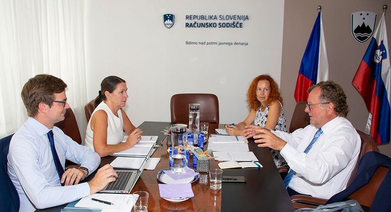 Fotografiji predsednikov in predstavnikov računskega sodišča in VRI Češke republike na enem izmed delovnih sestankov v okviru obiska, ki sedijo za mizo, v ozadju logotip in slogan računskega sodišča ter zastavi Češke republike in Slovenije