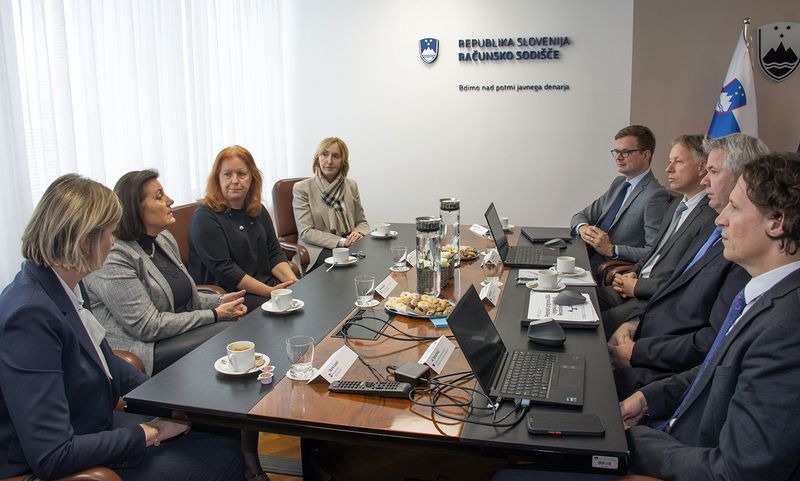 Predstavniki Računskega sodišča Republike Slovenije in delegacije vrhovne revizijske institucije (VRI) Hrvaške na bilateralnem delovnem sestanku v prostorih Računskega sodišča Republike Slovenije; udeleženci sedijo za konferenčno mizo, na kateri so prenosni računalniki, dokumenti in kava, na steni v ozadju pa je napis »Republika Slovenija – Računsko sodišče«.