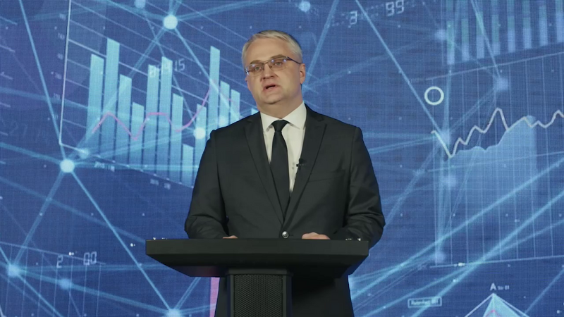 Glavni revizor Računskega sodišča Estonije in predsedujoči EUROSAI ITWG Janar Holm stoji za govorniškim pultom in nagovarja občinstvo; v ozadju so prikazi grafov in podatkovnih vizualizacij.