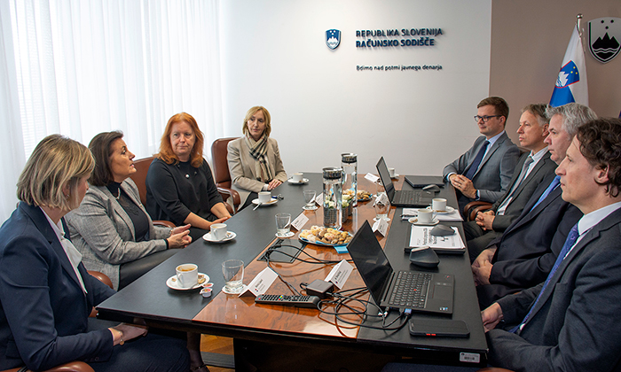 Predstavniki Računskega sodišča Republike Slovenije in delegacije vrhovne revizijske institucije (VRI) Hrvaške na bilateralnem delovnem sestanku v prostorih Računskega sodišča Republike Slovenije; udeleženci sedijo za konferenčno mizo, na kateri so prenosni računalniki, dokumenti in kava, na steni v ozadju pa je napis »Republika Slovenija – Računsko sodišče«.