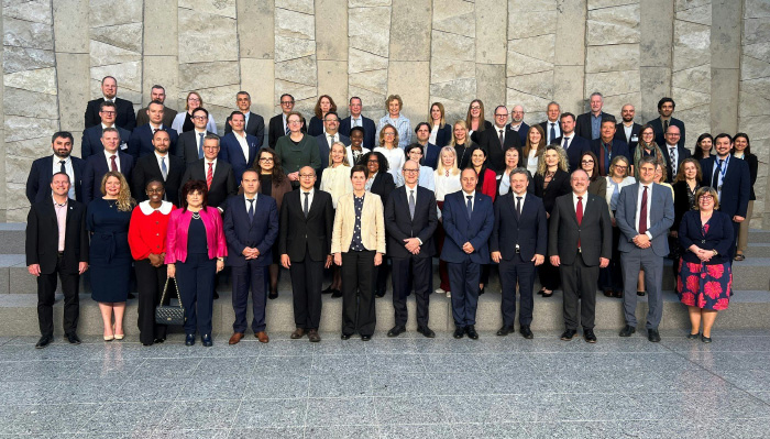 Skupinska fotografija udeležencev rednega srečanja predstavnikov pristojnih nacionalnih revizijskih organov (CNAB) in članov Mednarodnega revizijskega odbora za NATO (IBAN), ki je 21. maja 2026 potekalo na sedežu zveze NATO v Bruslju. Na fotografiji je približno 60 udeležencev, žensk in moških v poslovnih oblačilih, razporejenih v več vrstah na stopnicah pred veliko kamnito steno svetlih sivih tonov. V ospredju stojijo predstavniki različnih držav in institucij, med njimi tudi pomočnik vrhovne državne revizorke Računskega sodišča Republike Slovenije Viki Twrdy. Srečanje je bilo namenjeno predstavitvi dela odbora IBAN v preteklem letu ter razpravi o revizijah na področju obrambe, zaupnosti podatkov in mednarodnem sodelovanju vrhovnih revizijskih institucij.