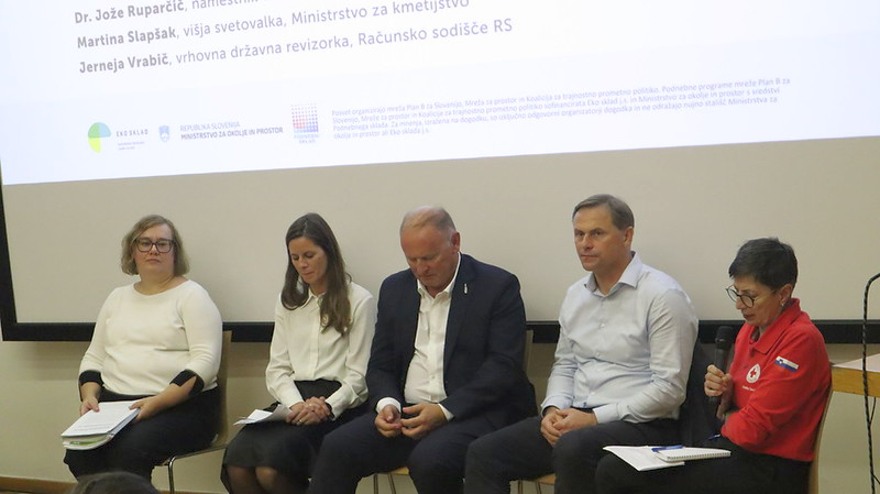 Pet udeležencev okrogle mize sedi na odru; udeleženka na desni drži mikrofon.